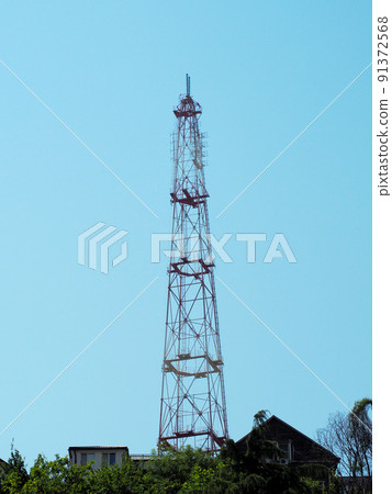 A tall cell tower rises above the rooftops of private houses against a blue sky. Selective focus A tall cell tower rises above the rooftops of private houses against a blue sky. Selective focus 91372568