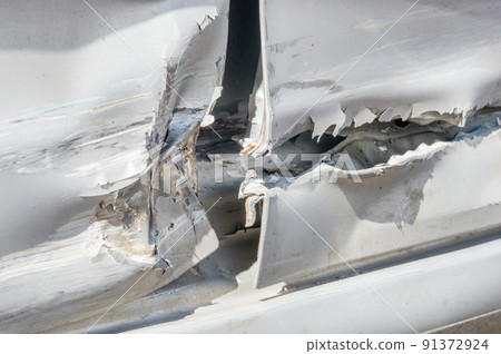 Detail of dented and torn sheet metal on the side of the silver car doors damaged in crash accident. 91372924
