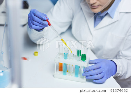 Close-up of busy female chemist in blue rubber gloves sitting at desk in laboratory 91374662