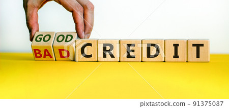 Male hand flips wooden cubes and changes the words 'bad credit' to 'good credit' or vice versa. Beautiful yellow table, white background, copy space. Business concept. 91375087