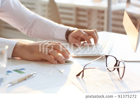 Close-up of unrecognizable male analyst in white shirt sitting at table in office and using computer while researching internet market Close-up of unrecognizable male analyst in white shirt sitting at table in office and using computer while researching internet market 91375272