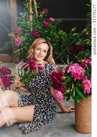 an attractive middle-aged blonde woman sits on the floor with flowers. 91376177