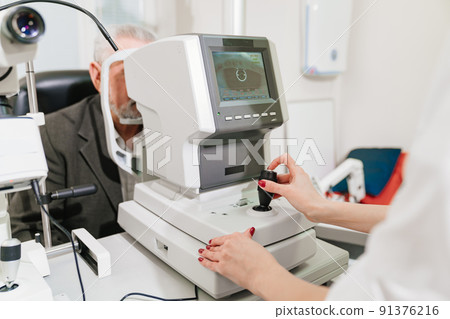 doctor examines elderly man's eye on screen of autorefractometer.  91376216