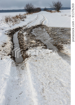 Snowy road in a field leading to pine forest. Winter road to nowhere in sunny day, snow-covered fresh car track. Car traces in a deep snow of remote rural area Snowy road in a field leading to pine forest. Winter road to nowhere in sunny day, snow-covered fresh car track. Car traces in a deep snow of remote rural area 91376269
