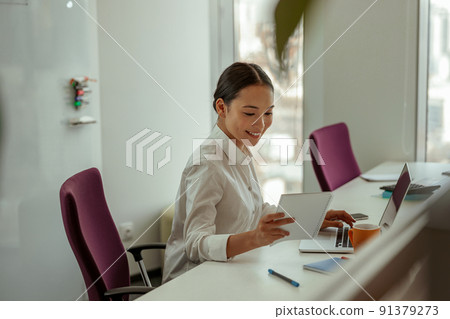 Asian business woman looking at her notes in notebook while working on laptop 91379273