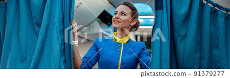 Joyful woman stewardess holding curtains in passenger aircraft 91379277