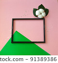 Summer modern composition. Black photo frame, green leaves and flower cotton of tree on pastel pink background. Flat lay, top view, copy space 91389386