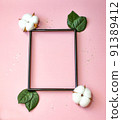 Summer modern composition. Black photo frame, green leaves and flower cotton of tree on pastel pink background. Flat lay, top view, copy space 91389412