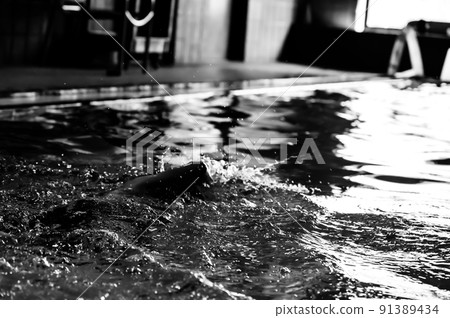 Youth swimming lesson in indoor pool. Swimmers backlit and silhouette with light reflecting off of water surface. Youth swimming lesson in indoor pool. Swimmers backlit and silhouette with light reflecting off of water surface. 91389434