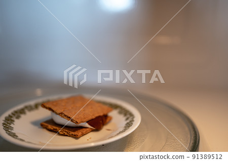 Making a smore with a marshmallow, cracker, and chocolate using a microwave. Making a smore with a marshmallow, cracker, and chocolate using a microwave. 91389512