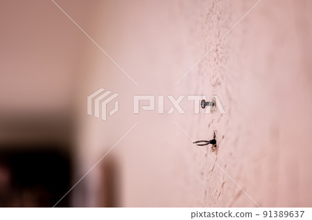 Selective focus on hole in a residential wall with two wires sticking out for surround sound speakers. 91389637