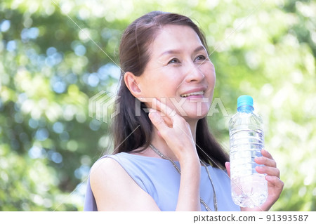 Senior woman hydrating in a midsummer park Senior woman hydrating in a midsummer park 91393587