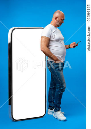 Middle-aged man standing and showing big smartphone with blank white screen Middle-aged man standing and showing big smartphone with blank white screen 91394165