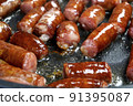 Delicious fatty hunting sausages, cut into pieces, are fried in frying pan in vegetable oil. Fast nutritious food. Home kitchen. Close-up. 91395087