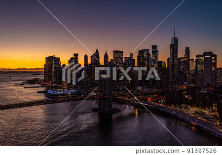 Beautiful aerial panoramic shot of downtown skyscrapers against golden sunset sky. Silhouettes of high rise office buildings with lighted windows. Manhattan, New York City, USA 91397526