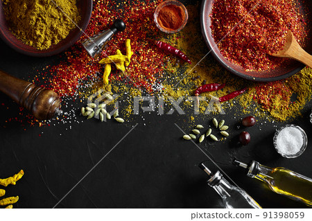 Cooking using fresh ground spices with big and small bowls of spice on a black table with powder spillage on its surface, overhead view with copyspace 91398059