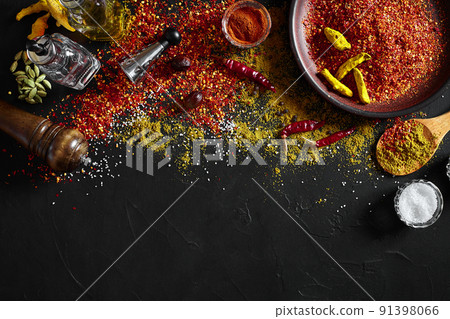 Cooking using fresh ground spices with big and small bowls of spice on a black table with powder spillage on its surface, overhead view with copyspace Cooking using fresh ground spices with big and small bowls of spice on a black table with powder spillage on its surface, overhead view with copyspace 91398066