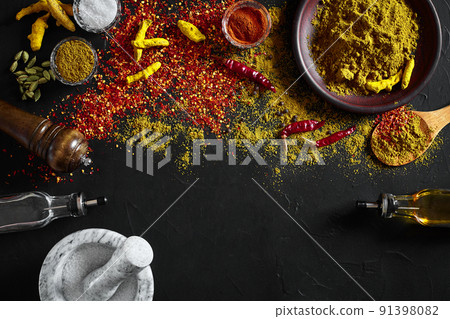 Cooking using fresh ground spices with mortar and small bowls of spice on a black table with powder spillage on its surface, overhead view with copyspace Cooking using fresh ground spices with mortar and small bowls of spice on a black table with powder spillage on its surface, overhead view with copyspace 91398082