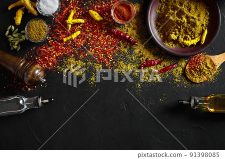 Cooking using fresh ground spices with big and small bowls of spice on a black table with powder spillage on its surface, overhead view with copyspace 91398085