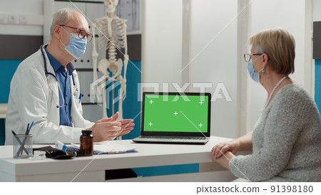 Doctor and retired patient using laptop with greenscreen at consultation appointment. Looking at isolated chroma key template with blank mockup and copy space background during pandemic. 91398180