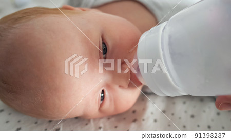 Newborn baby drinks water from plastic bottle lying on bed Newborn baby drinks water from plastic bottle lying on bed 91398287