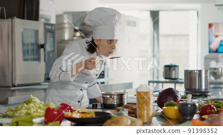 Authentic cook taste testing bad sauce on kitchen stove, preparing gourmet dish with delicious meal. Woman doing wrong culinary recipe for soup, making cuisine food preparations. 91398352