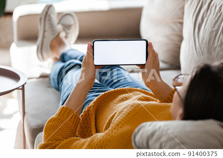 Young woman hold mobile phone screen mockup in hands, lying on the sofa Young woman hold mobile phone screen mockup in hands, lying on the sofa 91400375