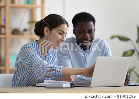 Two colleagues sit at desk with laptop discuss corporate software Two colleagues sit at desk with laptop discuss corporate software 91401289
