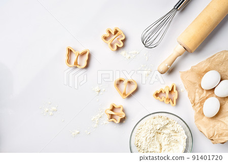 Bowl with wheat flour, rolling pin, whisk, eggs, cookie cutters. Top view on a white table with a copy space 91401720