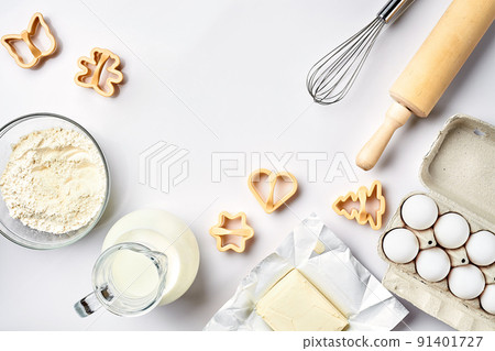 Objects and ingredients for baking, plastic molds for cookies on a white background. Flour, eggs, rolling pin, whisk, milk, butter, cream. Top view, space for text Objects and ingredients for baking, plastic molds for cookies on a white background. Flour, eggs, rolling pin, whisk, milk, butter, cream. Top view, space for text 91401727