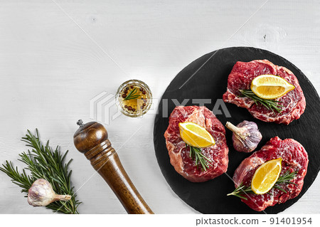 Fresh raw beef steaks with herbs, garlic, olive oil, pepper, salt and rosemary on black board: Tenderloin, Striploin, Rib Eye 91401954