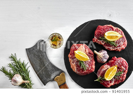 Fresh raw beef steaks with herbs, garlic, olive oil, pepper, salt and rosemary on black board: Tenderloin, Striploin, Rib Eye 91401955