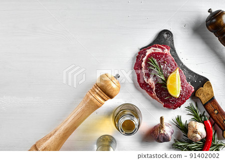 Fresh raw steaks with herbs, garlic, olive oil, pepper, salt, rosemary and a kitchen ax on white background. Top view. Fresh raw steaks with herbs, garlic, olive oil, pepper, salt, rosemary and a kitchen ax on white background. Top view. 91402002