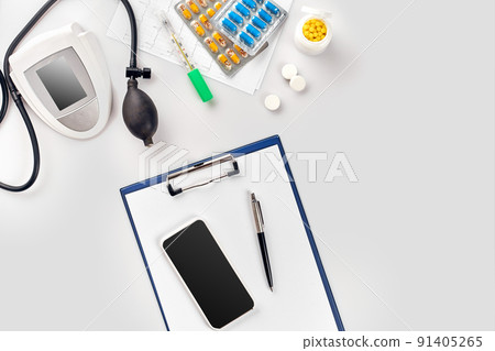 Top view of doctor's desk table, blank paper on clipboard with pen, electronic manometer to measure the blood pressure. 91405265