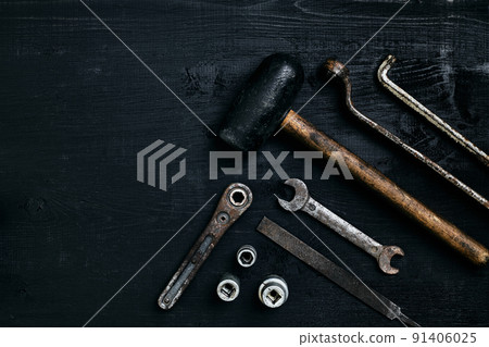Old, rusty tools lying on a black wooden table. Hammer, chisel, metal scissors, wrench. 91406025