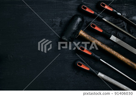 Series of many sharp steel blades and hammer on black wooden background Series of many sharp steel blades and hammer on black wooden background 91406030