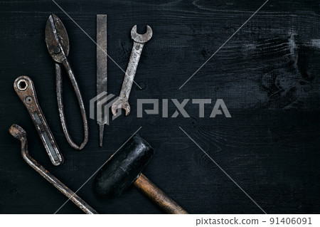 Old, rusty tools lying on a black wooden table. Hammer, chisel, metal scissors, wrench. 91406091