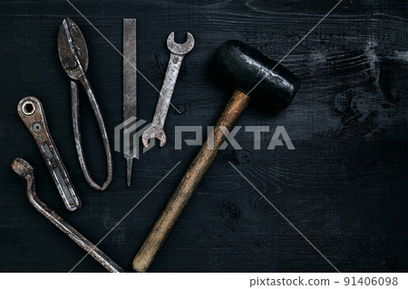 Old, rusty tools lying on a black wooden table. Hammer, chisel, metal scissors, wrench. 91406098