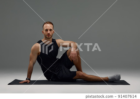 Confident young fitness man exercising on a fitness mat indoors, over gray wall background 91407614