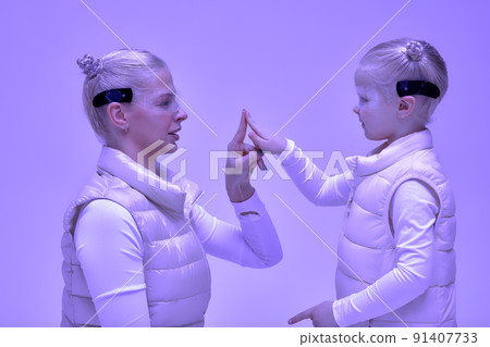 Woman with little girl in futuristic costume wearing smart led glasses of virtual reality while touching air. Augmented reality game, future technology, AI concept. VR. Neon light. Woman with little girl in futuristic costume wearing smart led glasses of virtual reality while touching air. Augmented reality game, future technology, AI concept. VR. Neon light. 91407733