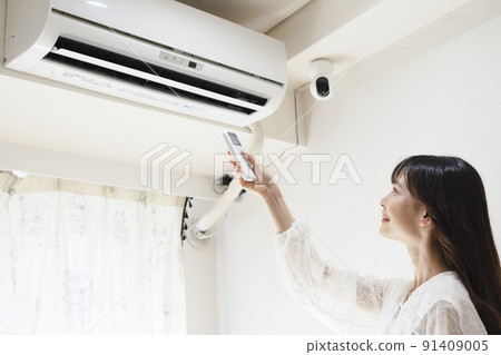 Woman turning on the air conditioner Woman turning on the air conditioner 91409005