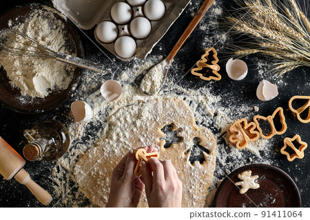 Close-up of a woman's hand with a dough. The woman is cutting a cookie with a cookie cutter in the shape of a little human. View from above. 91411064