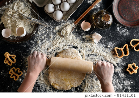 Female hands rolling dough with a rolling pin on a black table. Top view 91411101