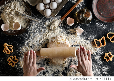 Female hands rolling dough with a rolling pin on a black table. Top view 91411114