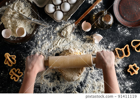 Female hands rolling dough with a rolling pin on a black table. Top view 91411119