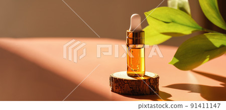 Cosmetic amber glass dropper bottle on wooden podium with oil, serum or fruit peeling in the sunlight. Green ruscus, soft focus. Beauty product presentation, natural background. Front. Mockup concept  91411147