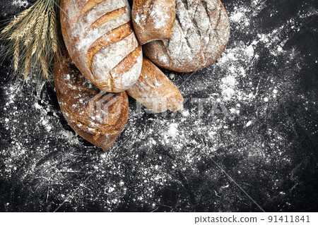 Homemade rye bread sprinkled with flour and various grains and seeds on a black background with spikelets of wheat or rye and oats. Homemade rye bread sprinkled with flour and various grains and seeds on a black background with spikelets of wheat or rye and oats. 91411841
