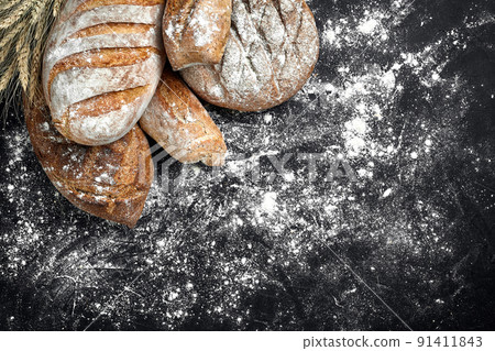 Homemade rye bread sprinkled with flour and various grains and seeds on a black background with spikelets of wheat or rye and oats. Homemade rye bread sprinkled with flour and various grains and seeds on a black background with spikelets of wheat or rye and oats. 91411843