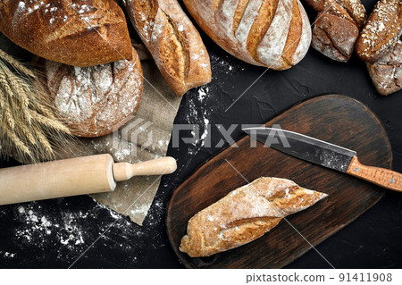 Fresh bread, wooden board and cutting knife on black table 91411908