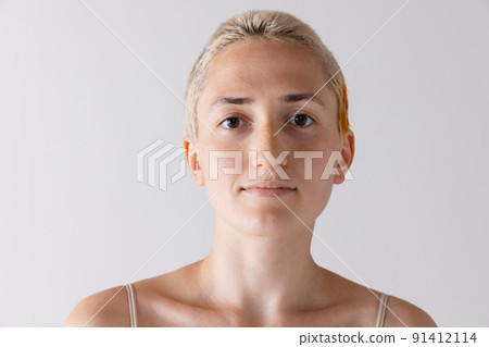 Portrait of young short-haired blonde girl posing, looking at camera isolated over grey studio background. Calmness Portrait of young short-haired blonde girl posing, looking at camera isolated over grey studio background. Calmness 91412114